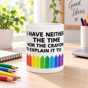 White rainbow crayon quote mug on a wooden desk beside coloured pencils and a notebook.