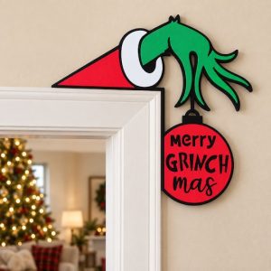 Merry Grinchmas decoration fitted over the top-right corner of a white door frame, with a Christmas tree beyond.